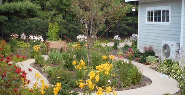 Colorful garden with a winding path beside a light-blue building and bench.