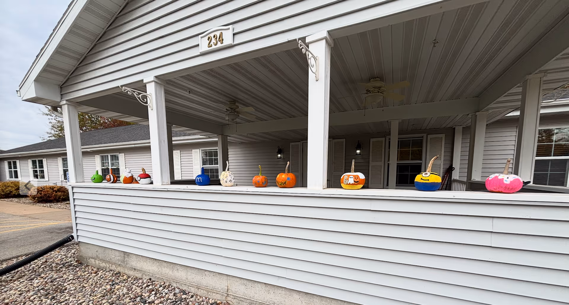 White, single-story building with a covered porch and colorful pumpkins along the railing.