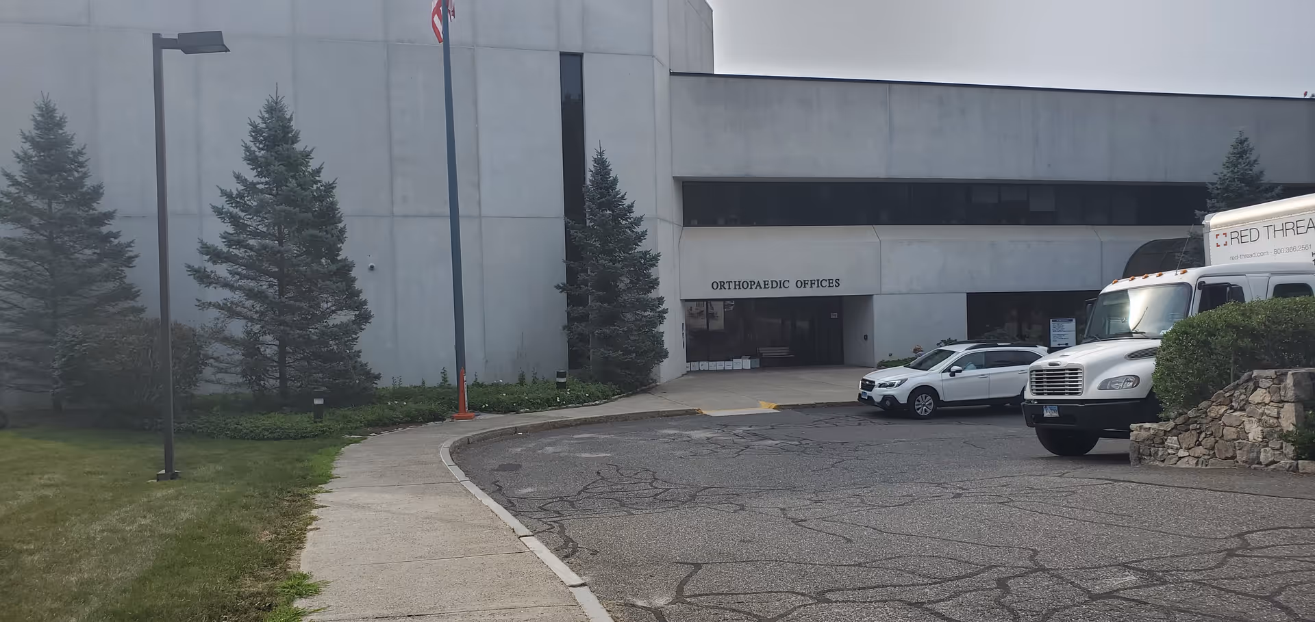 Exterior view of a medical building entrance with an Orthopaedic Offices sign and parked vehicles.