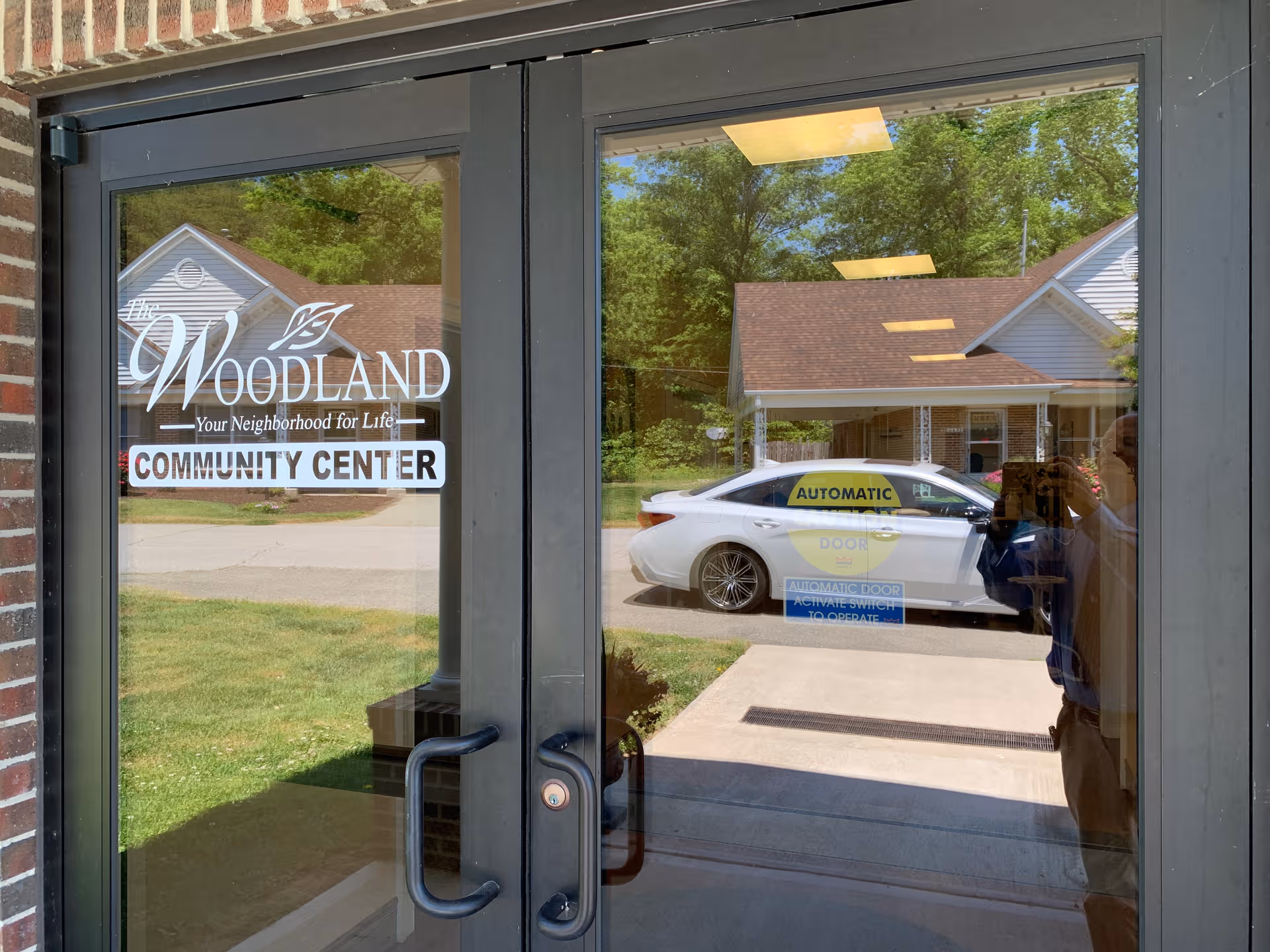 Glass entrance doors show The Woodland Community Center sign with a car parked outside.