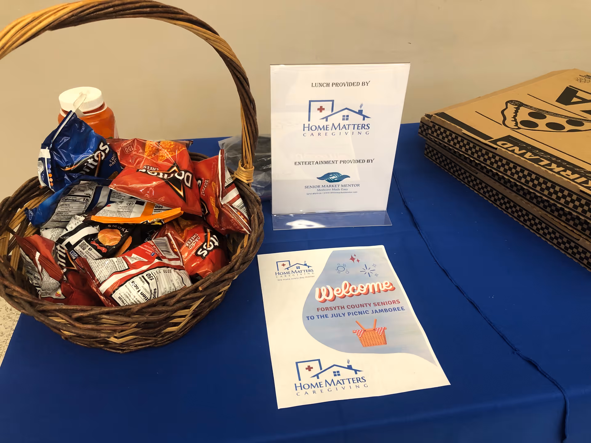 Basket of assorted chips on a blue table alongside Home Matters Caregiving sign and welcome flyer.