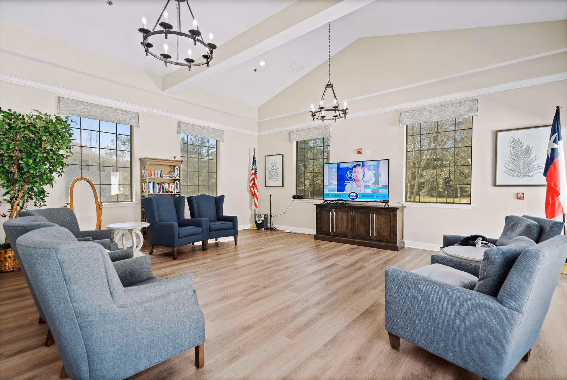 Senior living lounge with blue seating around a TV, American and Texas flags, and large windows.