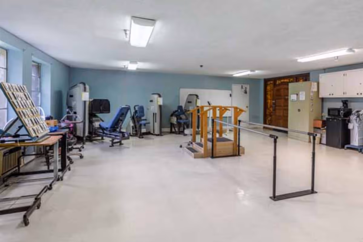 Rehab gym inside Harborview Thomasville featuring parallel bars, exercise machines, and cabinets.