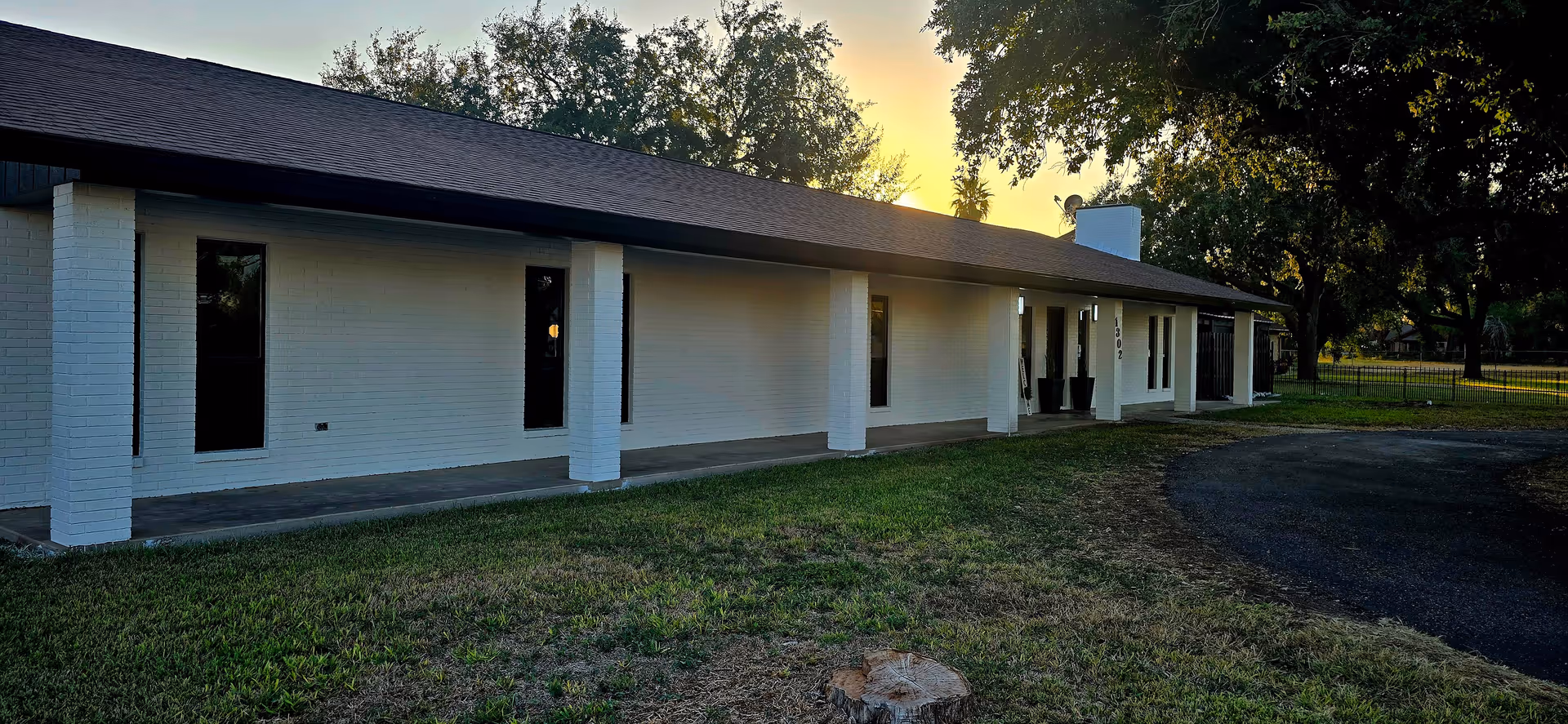 A single-story white facility exterior with columns, windows, and a curved driveway at sunset