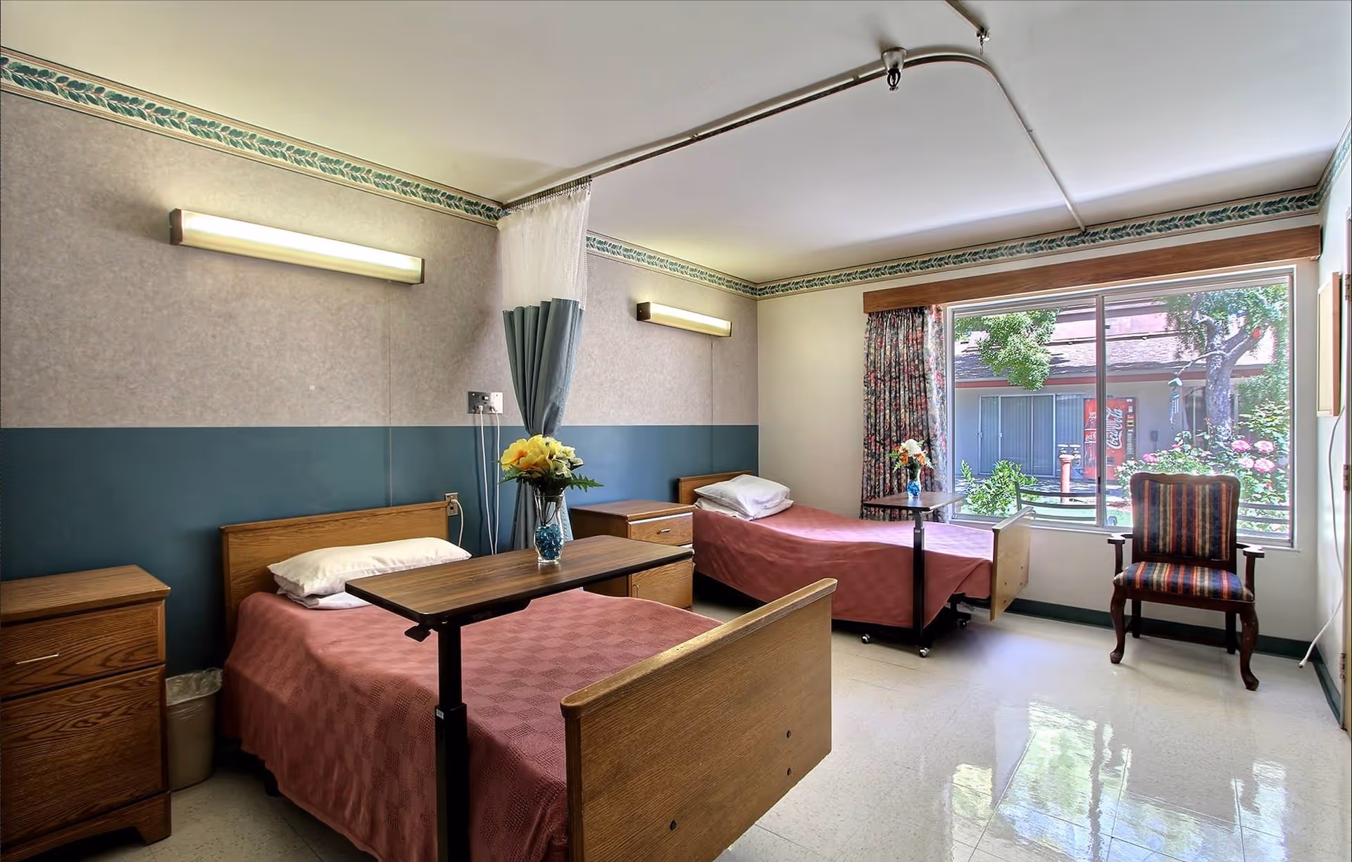 Two single beds with pink bedspreads, nightstands, and a central table between them.