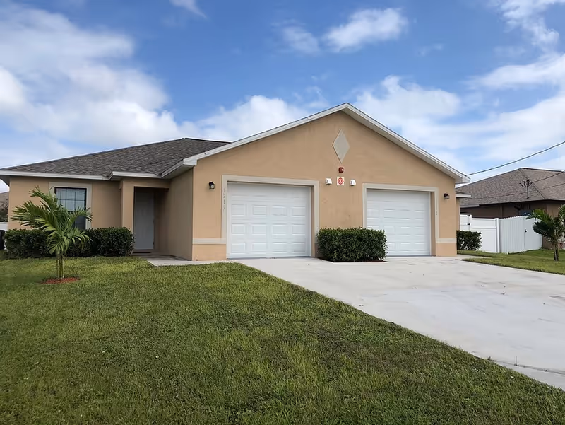Beige single-story facility with two white garage doors, driveway, and green lawn under blue sky.