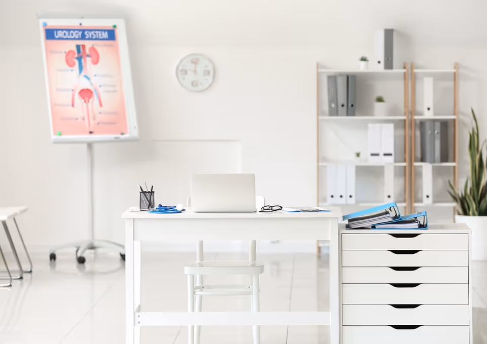 Bright white clinic office with desk, laptop, shelves, and a filing cabinet.