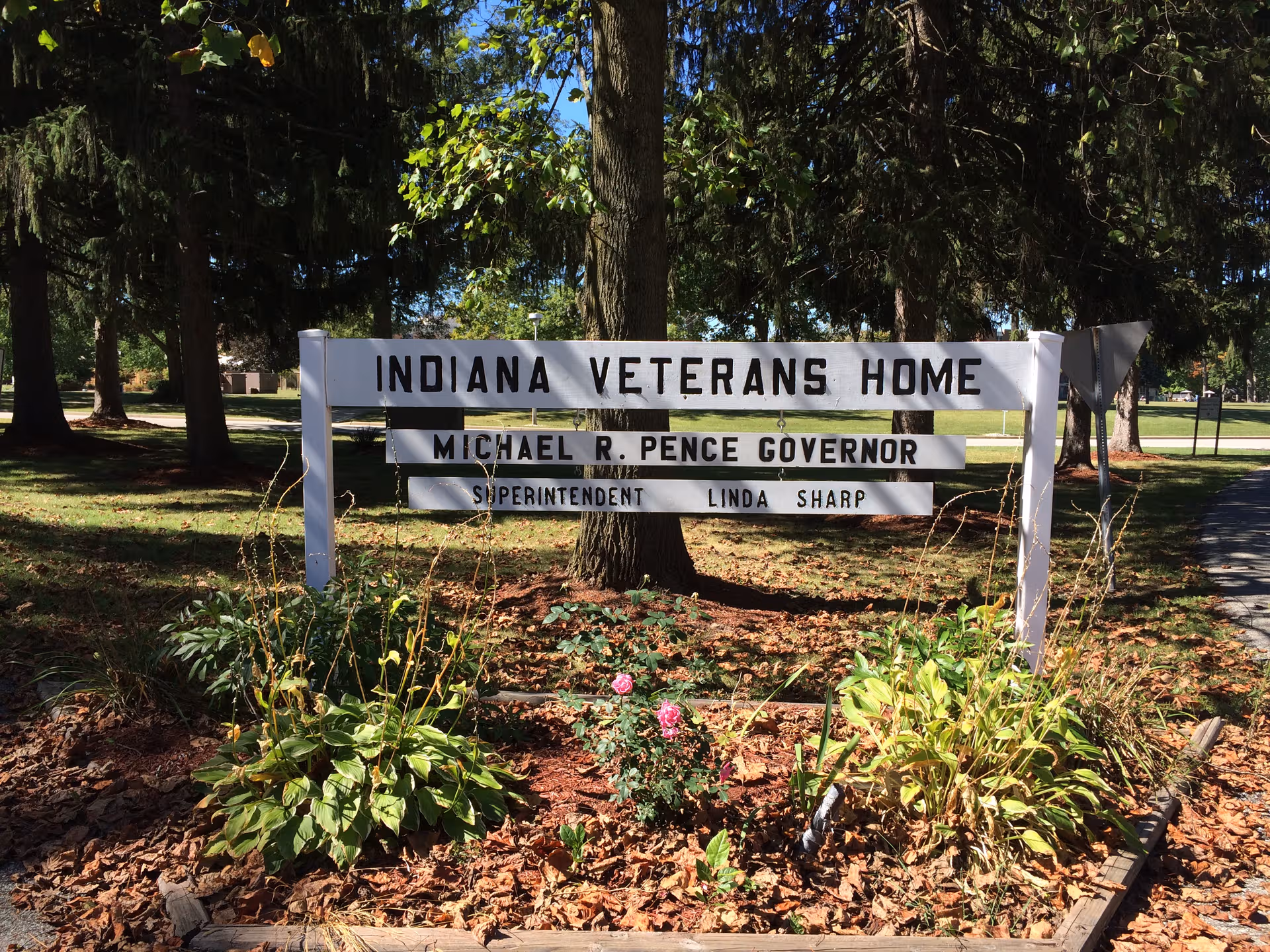 Outdoor sign reading Indiana Veterans Home with surrounding landscaping and tall trees.
