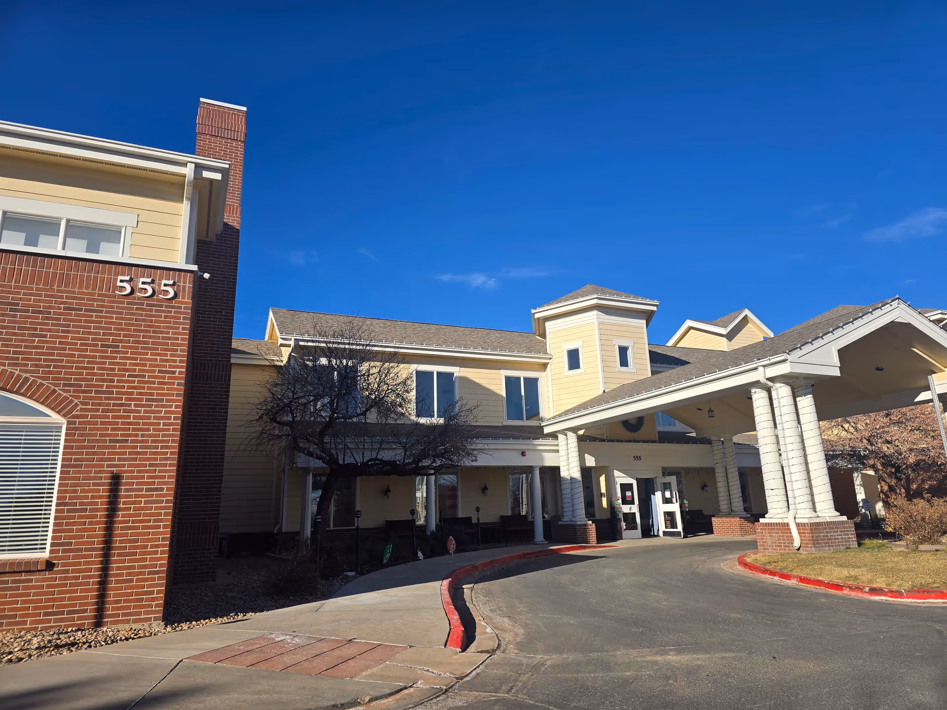 Exterior front view of Lakewood Reserve Assisted Living & Memory Care building with a covered entrance, brick and yellow siding facade, and clear blue sky.