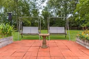 Red brick patio with a double outdoor swing and pedestal table amid planters and trees.