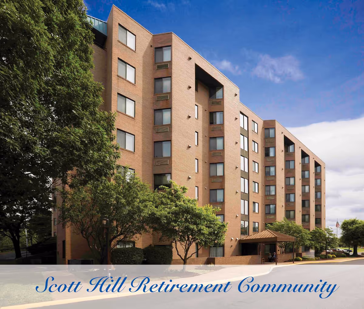 Exterior view of a multi-story brick building with many windows, surrounded by trees and greenery under a partly cloudy blue sky. The building has an entrance with a covered awning. Text at the bottom reads 'Scott Hill Retirement Community'.