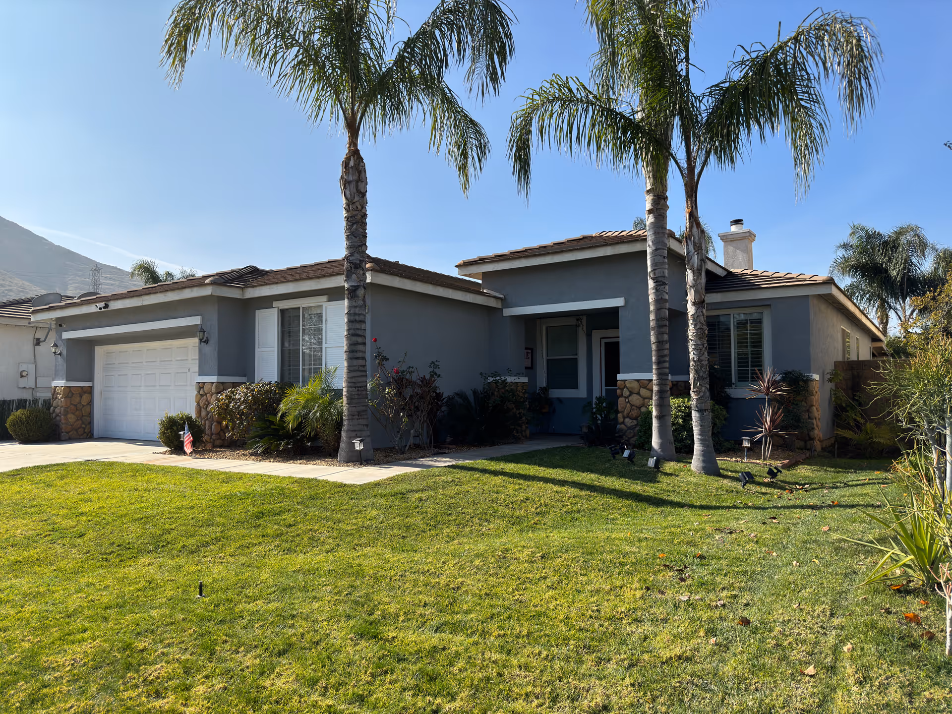 Front exterior of Magnolia Gardens: a single-story building with a garage, palm trees, and a lawn.
