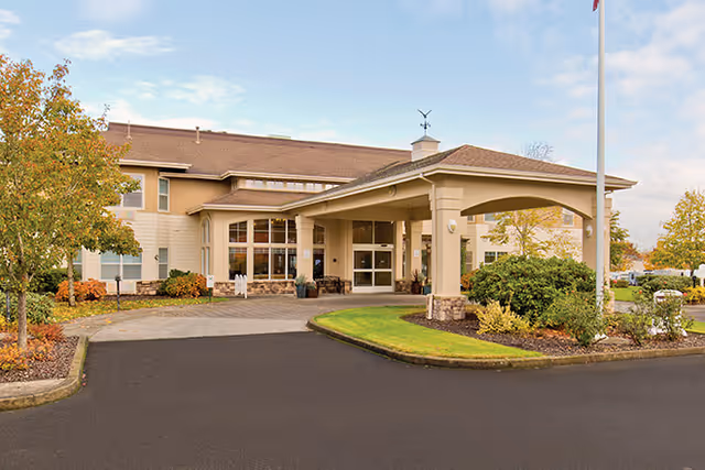 Senior living facility exterior with a covered entrance and landscaped driveway.