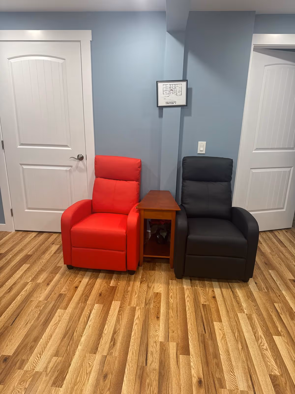 Two upholstered armchairs, red and black, flank a small wooden table in a blue-walled living area.
