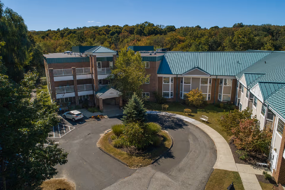 Aerial view of a multi-wing assisted living facility with teal roofs and circular driveway.