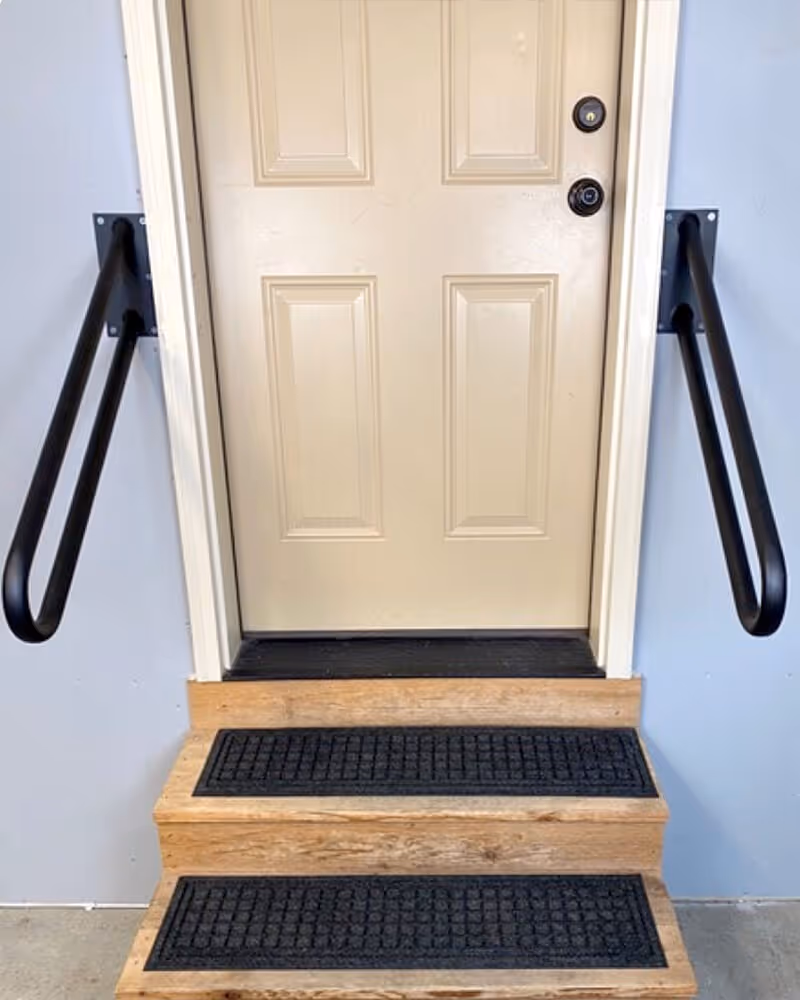 Beige entry door at top of wooden stairs with black handrails inside a facility.