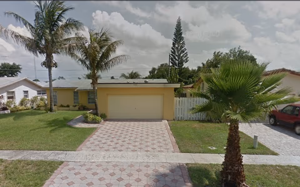 Front exterior of Paradise Villas Retirement with a garage, palm trees, and a tiled driveway.