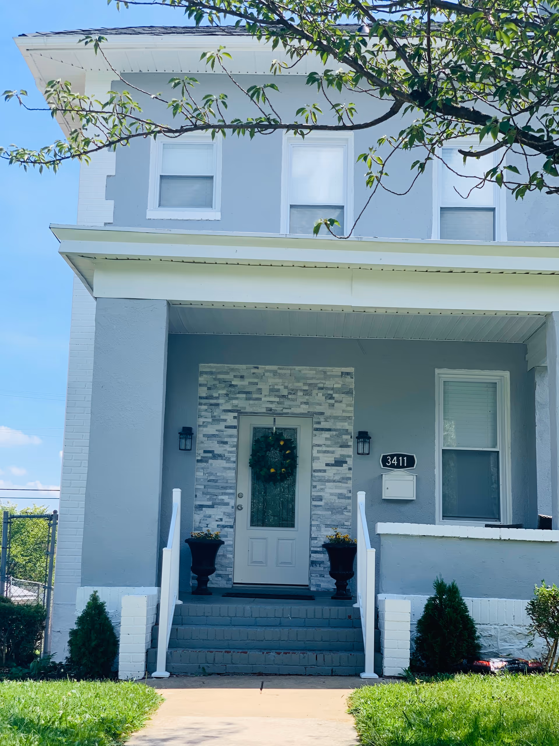 Light blue two-story building with a front porch, steps, and decorative wreath at entry.