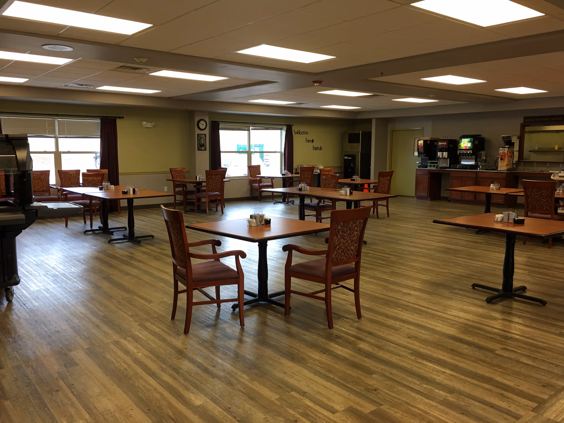 Large communal dining area with multiple tables, chairs, and a beverage station along the wall.