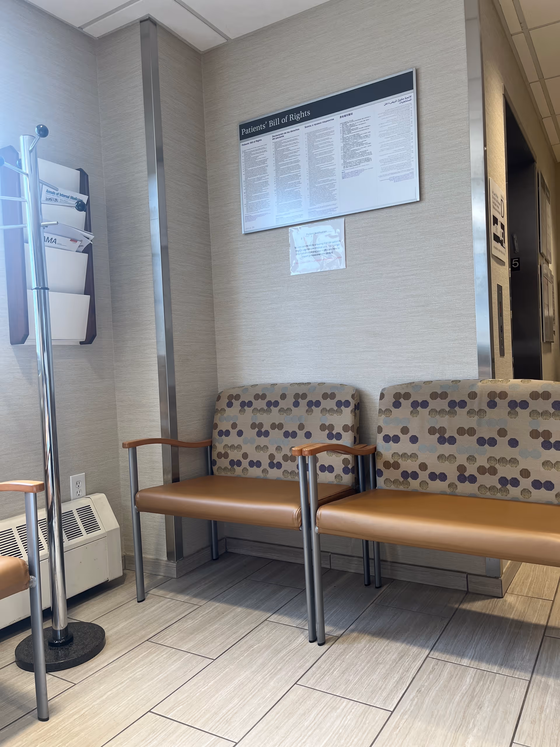 Hospital waiting area with patterned chairs, a wall sign, and a magazine rack in a lobby.