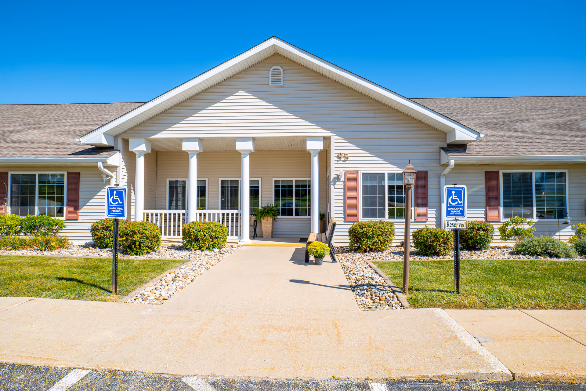 Front exterior of Arlington Place at Grundy Center with entrance, columns, and landscaped walkway.