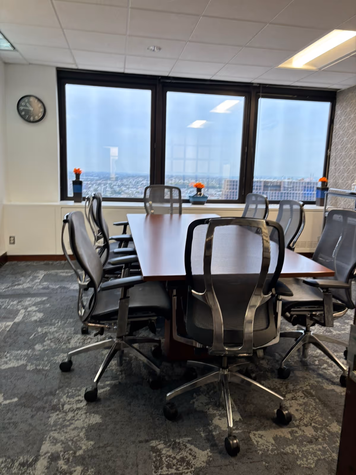 A conference table with multiple chairs in a bright office-style interior overlooking a city.