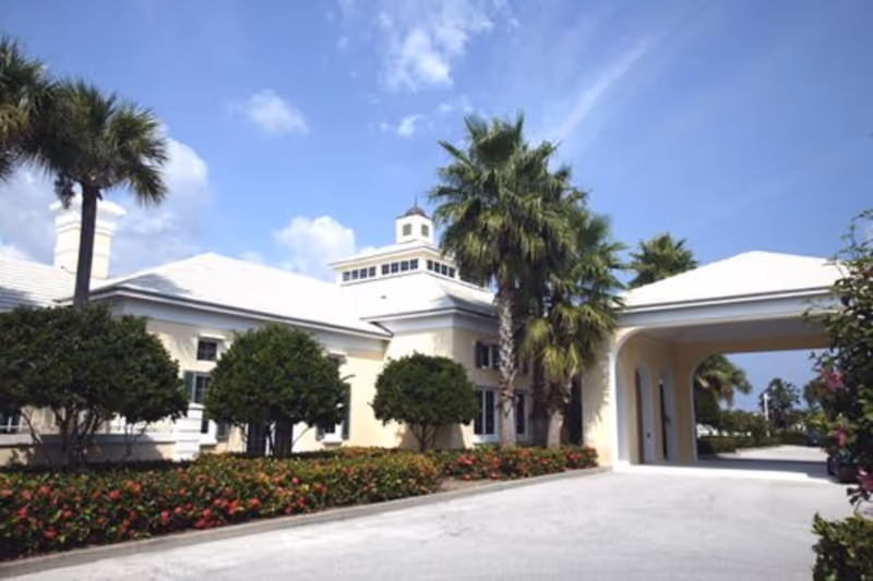 White senior living facility with palm trees and a covered entrance.