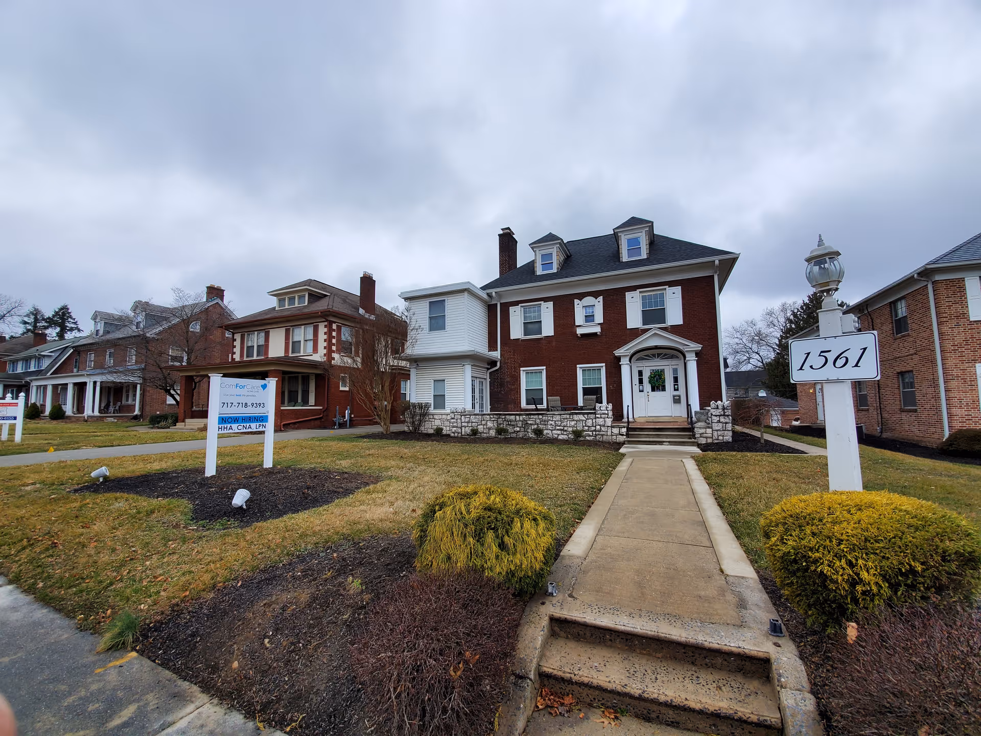 Front exterior of a brick senior living building with a walkway and address sign.