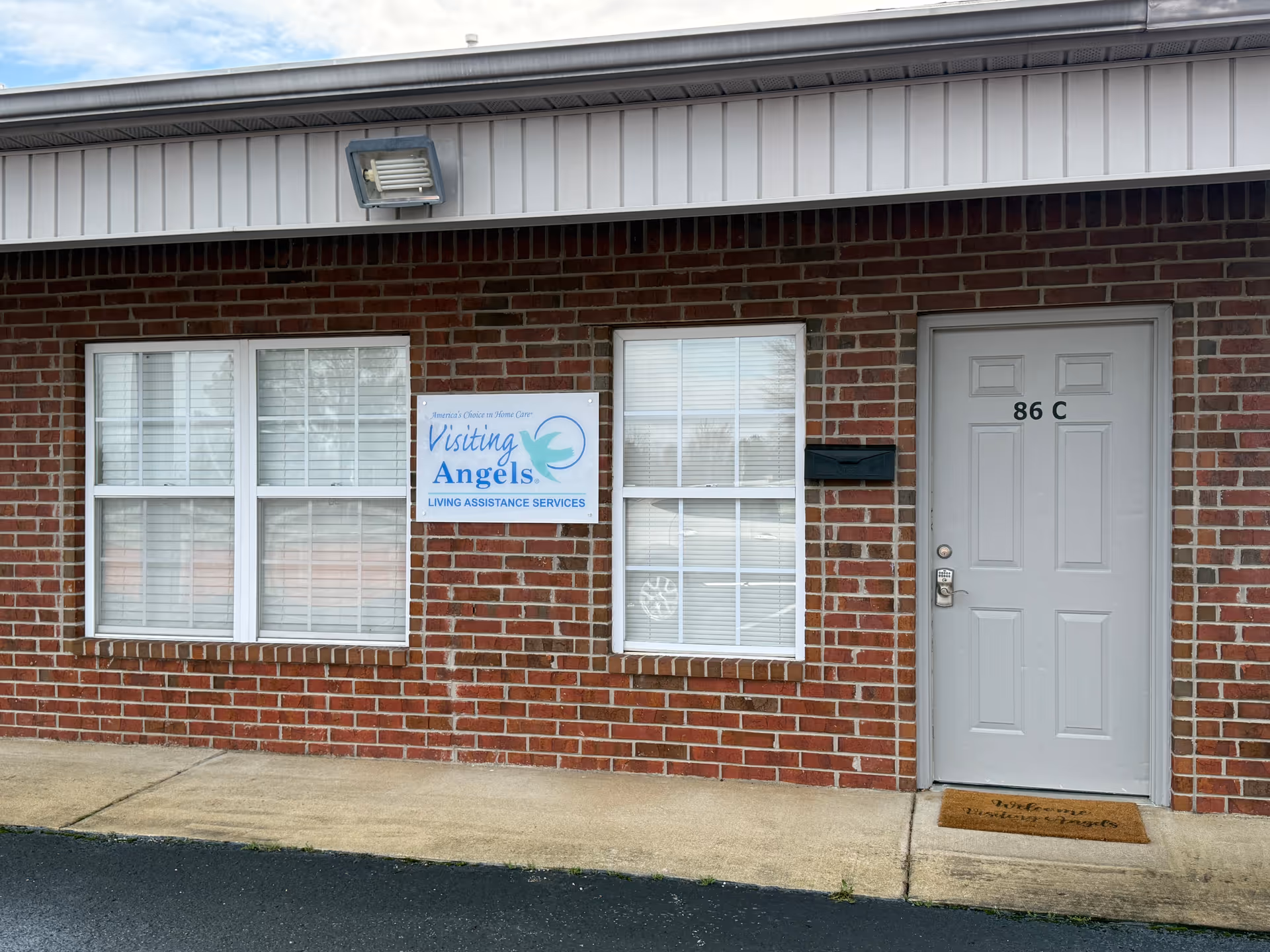 Brick building exterior with a gray door labeled 86 C and a Visiting Angels sign.