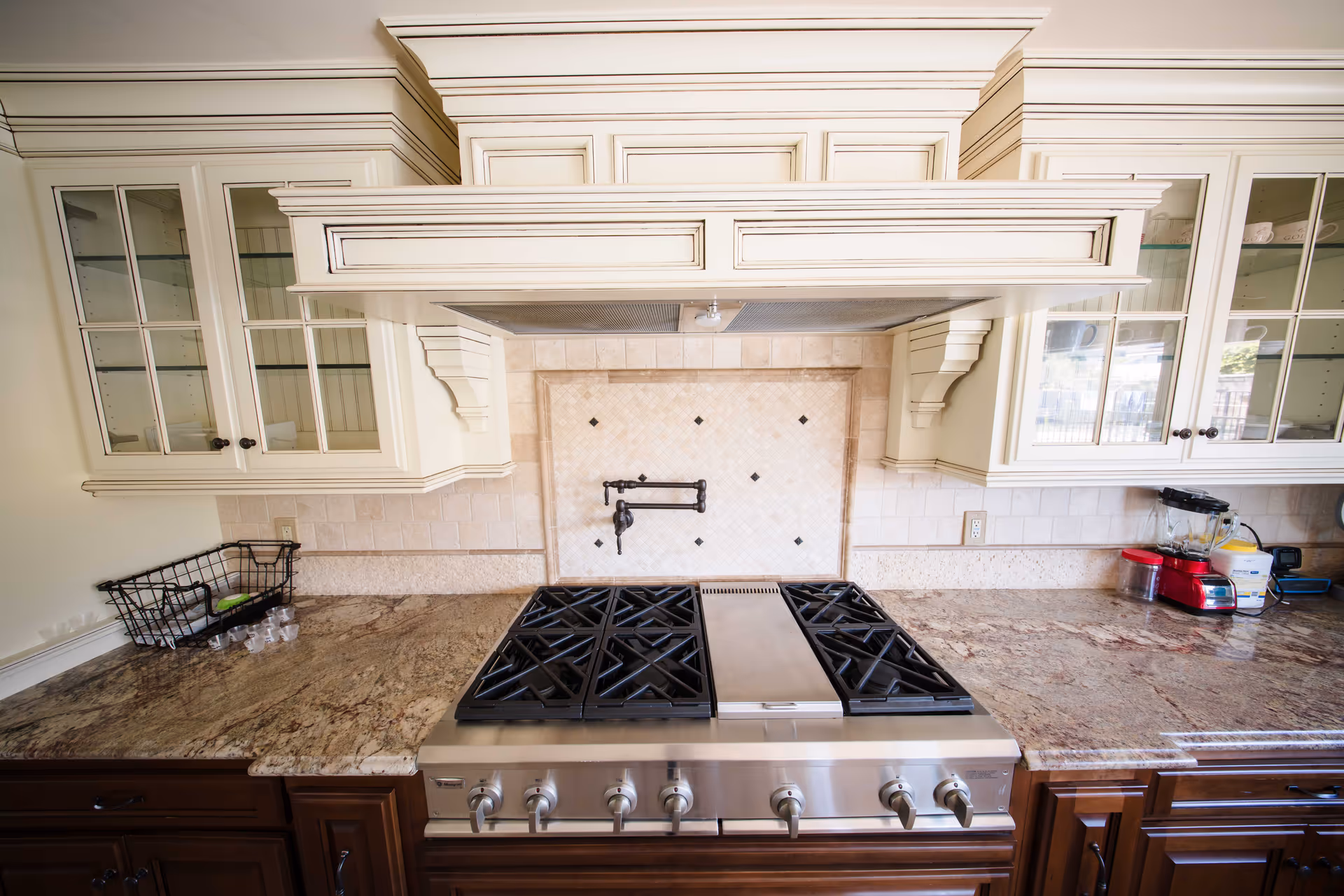A clean kitchen with a stainless stove, granite countertops, and cream cabinets.