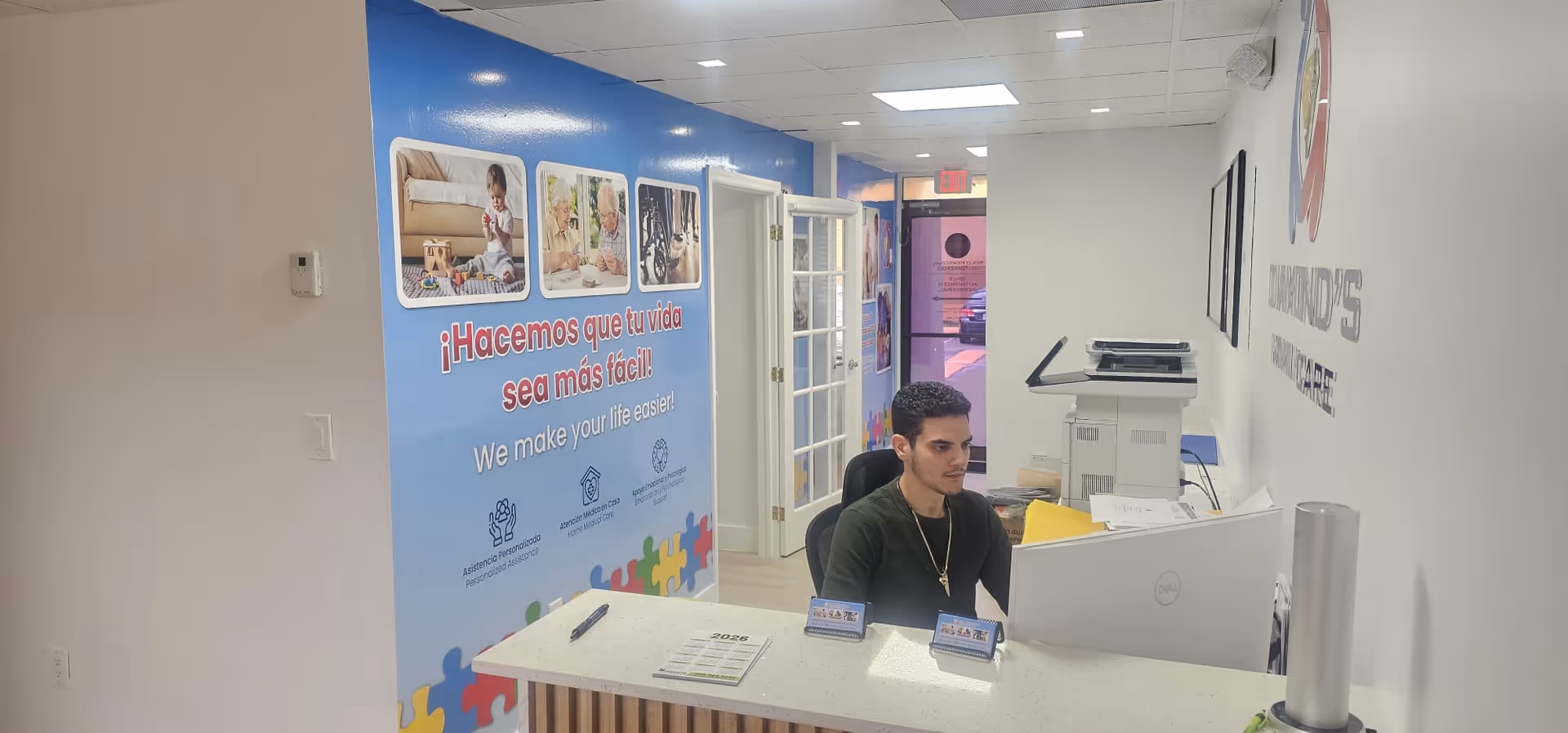 Reception area with a man at a computer behind a white counter in a facility lobby.