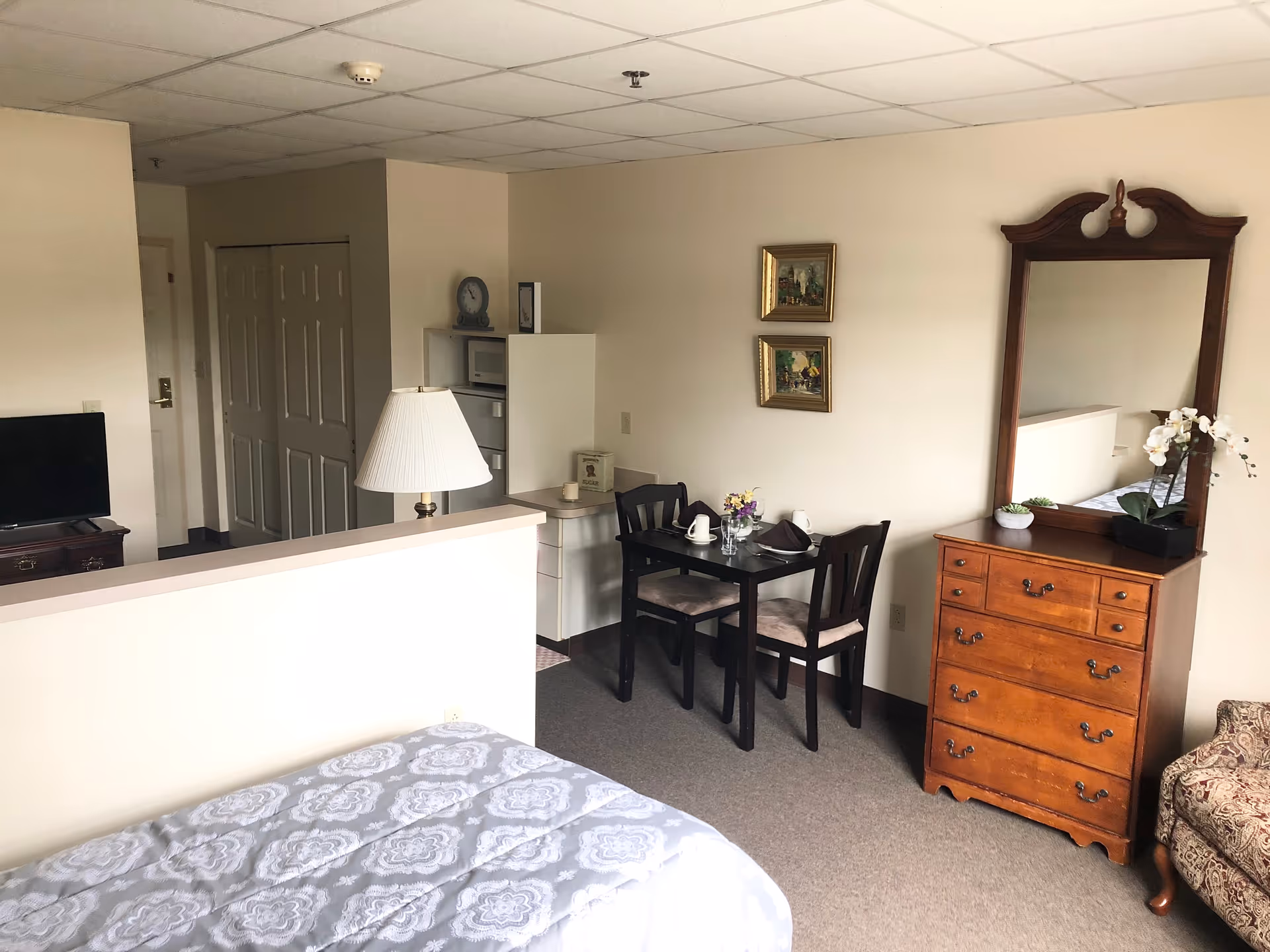Cozy senior living bedroom with bed, dining table, and wooden dresser.