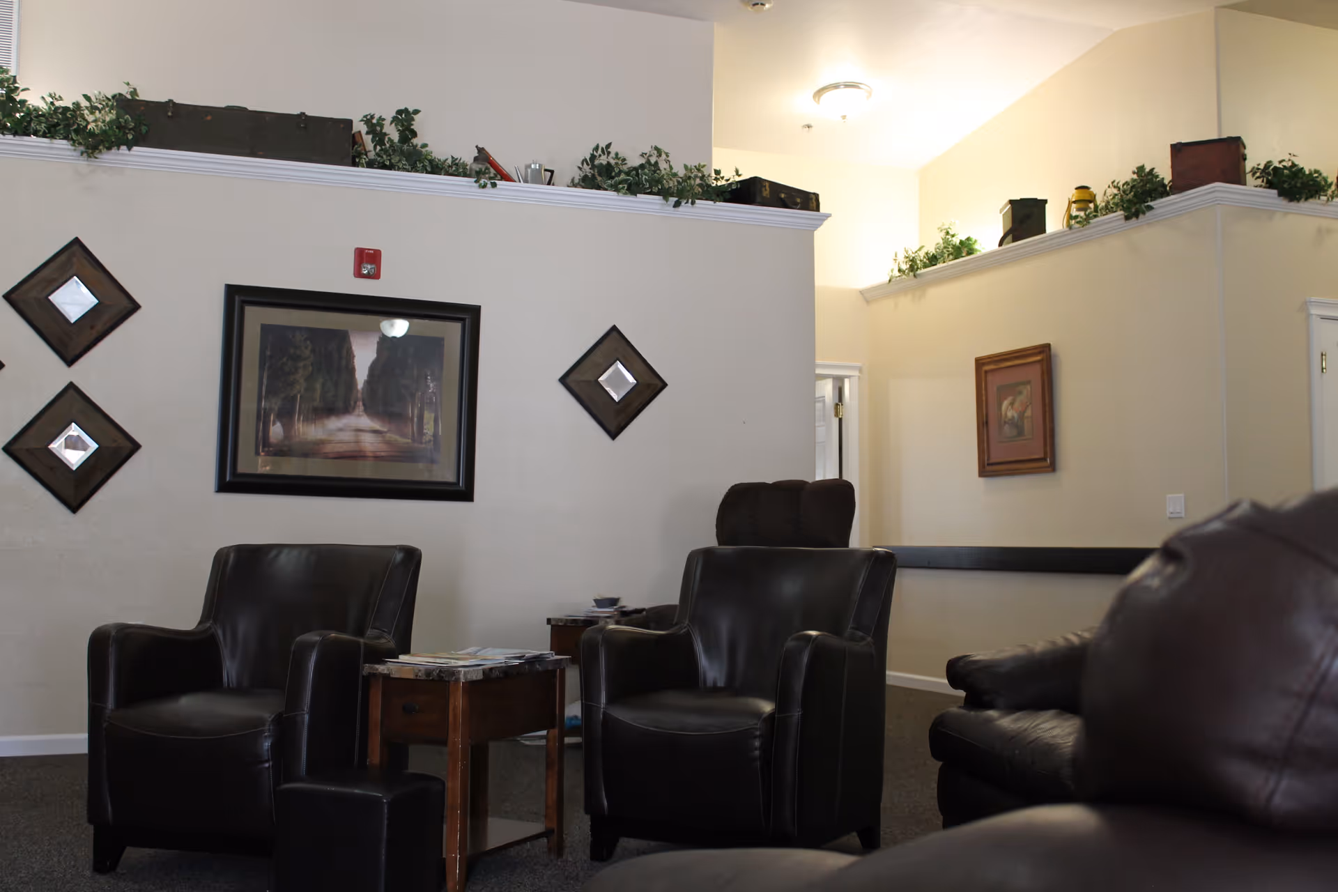 Interior lounge with black leather chairs, a wooden side table, wall art, and greenery.