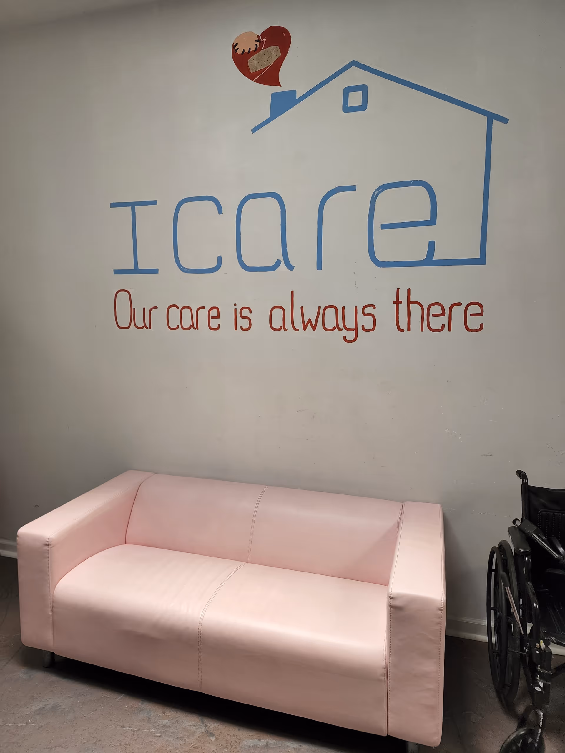 Light pink sofa beside a wheelchair, against a wall with Icare logo and slogan.