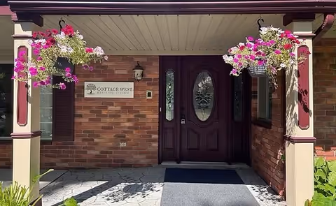 Brick exterior entrance with double dark doors, hanging flower baskets, and a sign.