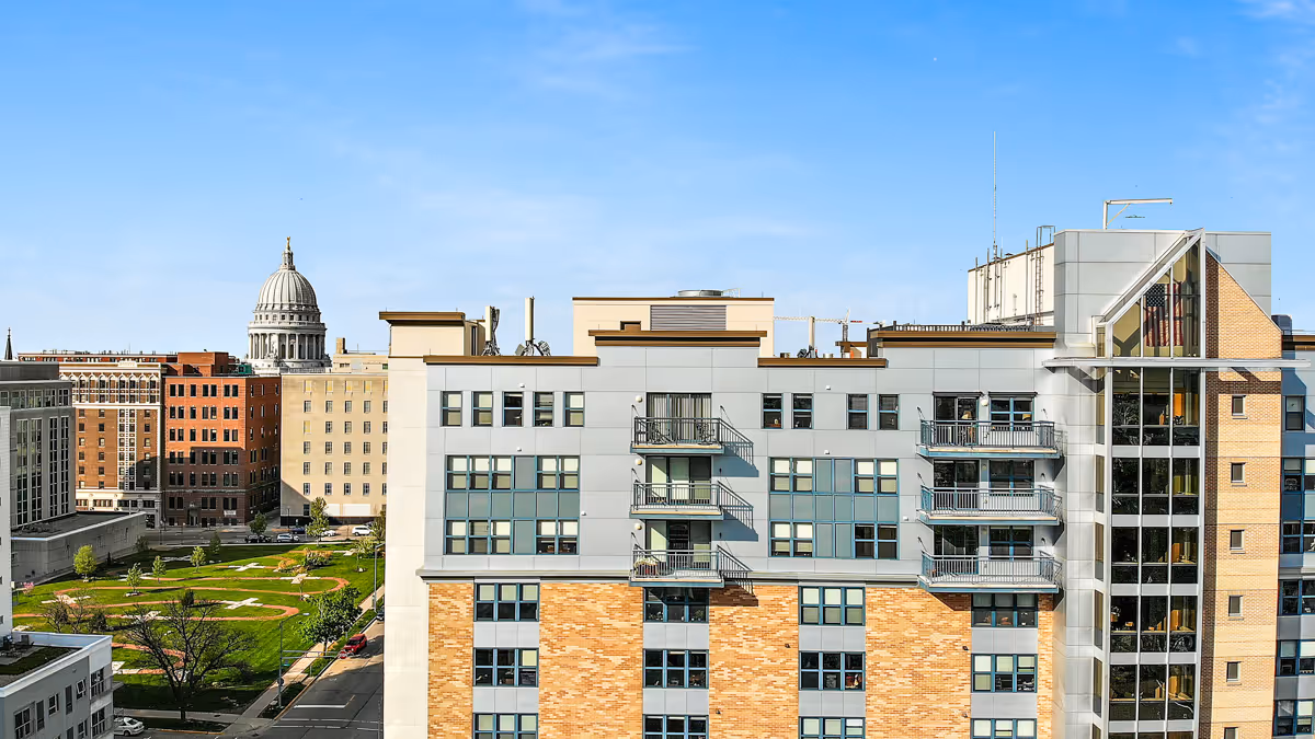 Modern senior living building with balconies, green park, and city skyline backdrop.