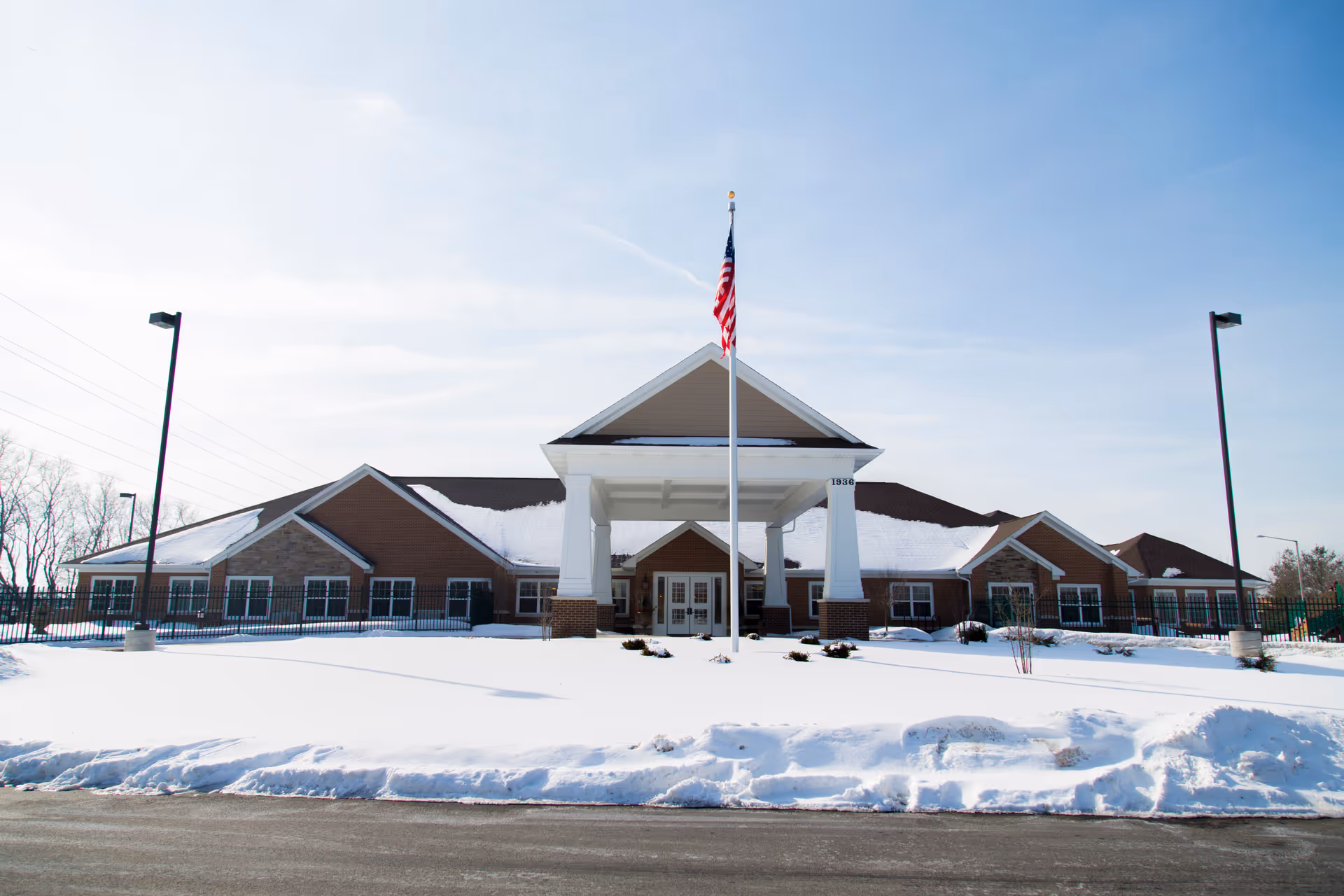 Snow-covered exterior of The Auberge at Naperville with a front entrance and flagpole.