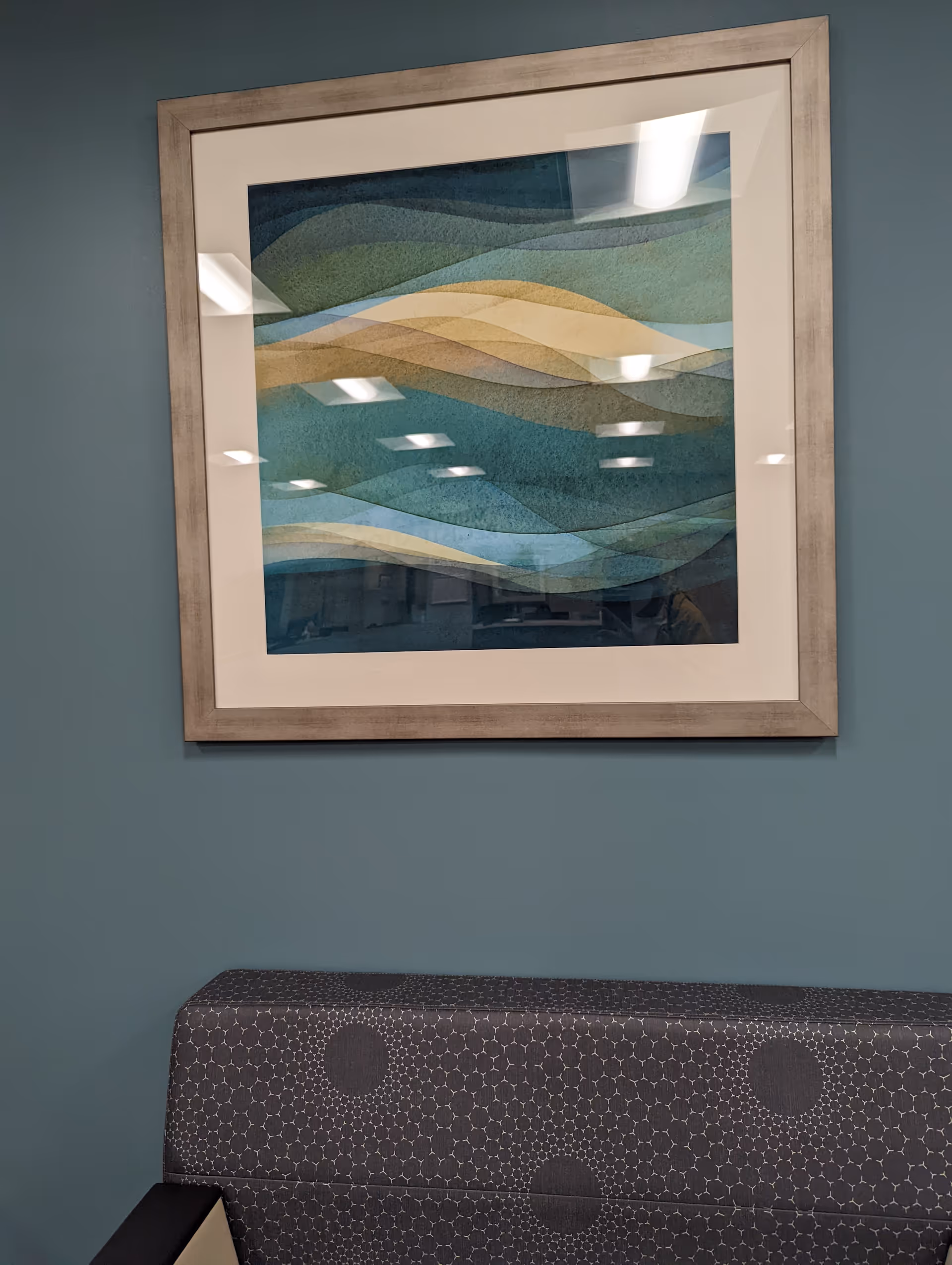 Teal wall with a framed abstract artwork above a patterned upholstered bench.