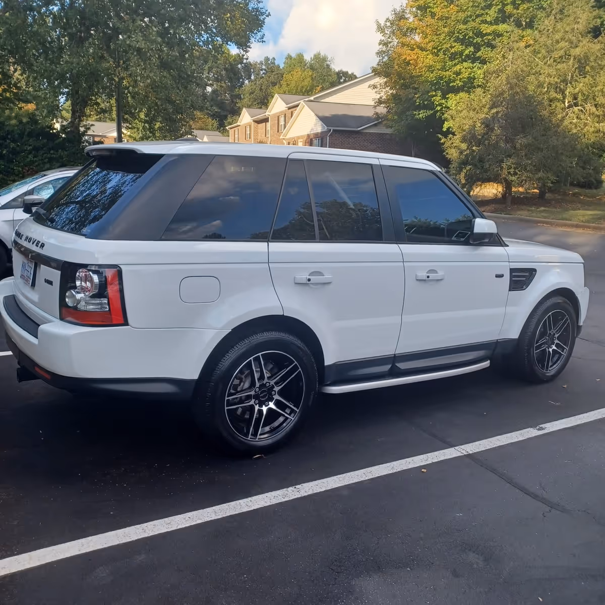 White Range Rover SUV parked in a paved lot with trees and a brick building behind.