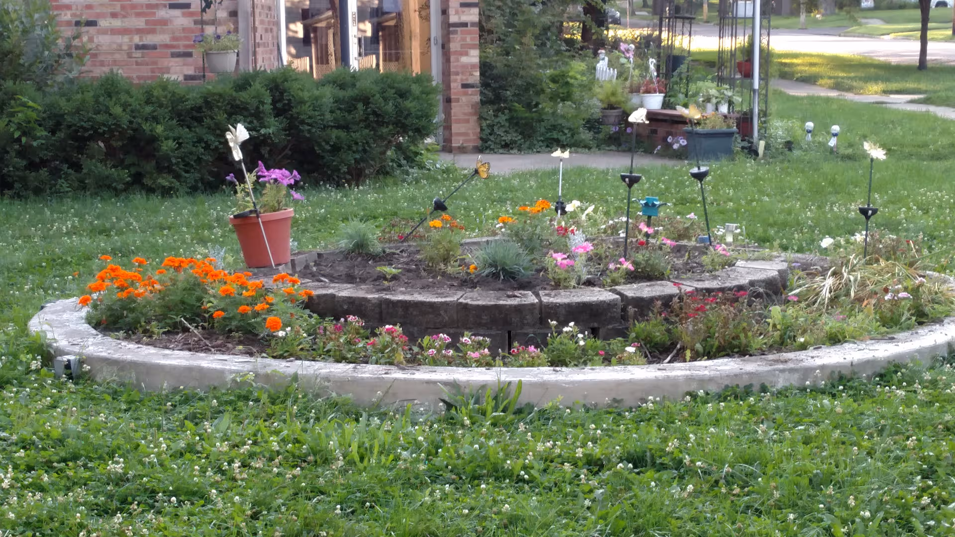 Circular raised flower bed with colorful blooms in front of a brick building.