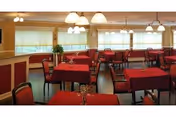 A dining room with red tablecloths, chairs, and large windows under warm lighting.