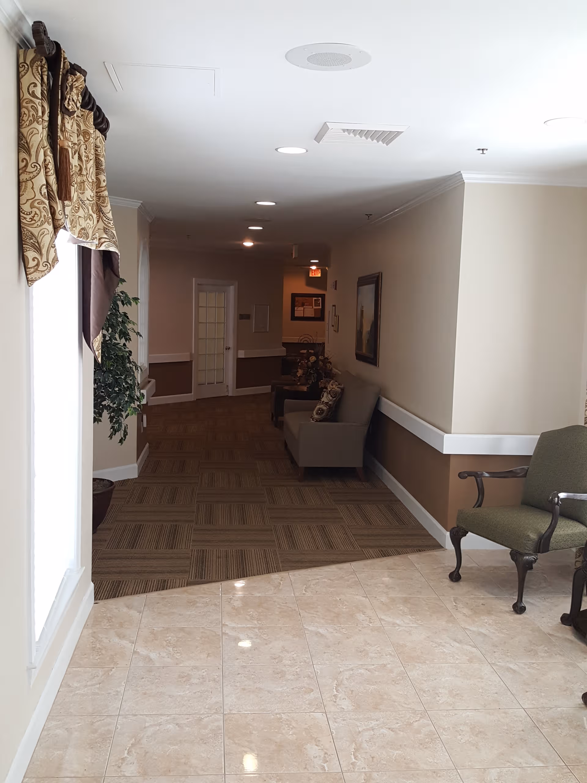 Interior senior living lobby with beige walls, tiled floor, and seating along the hallway.