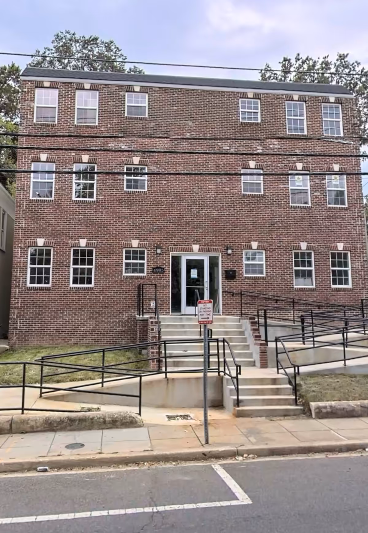Brick three-story building with stairs and ramps leading to a central entrance.