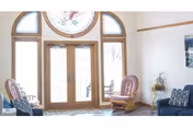Sunlit interior lobby with arched glass doors, wooden frames, and cushioned seating.