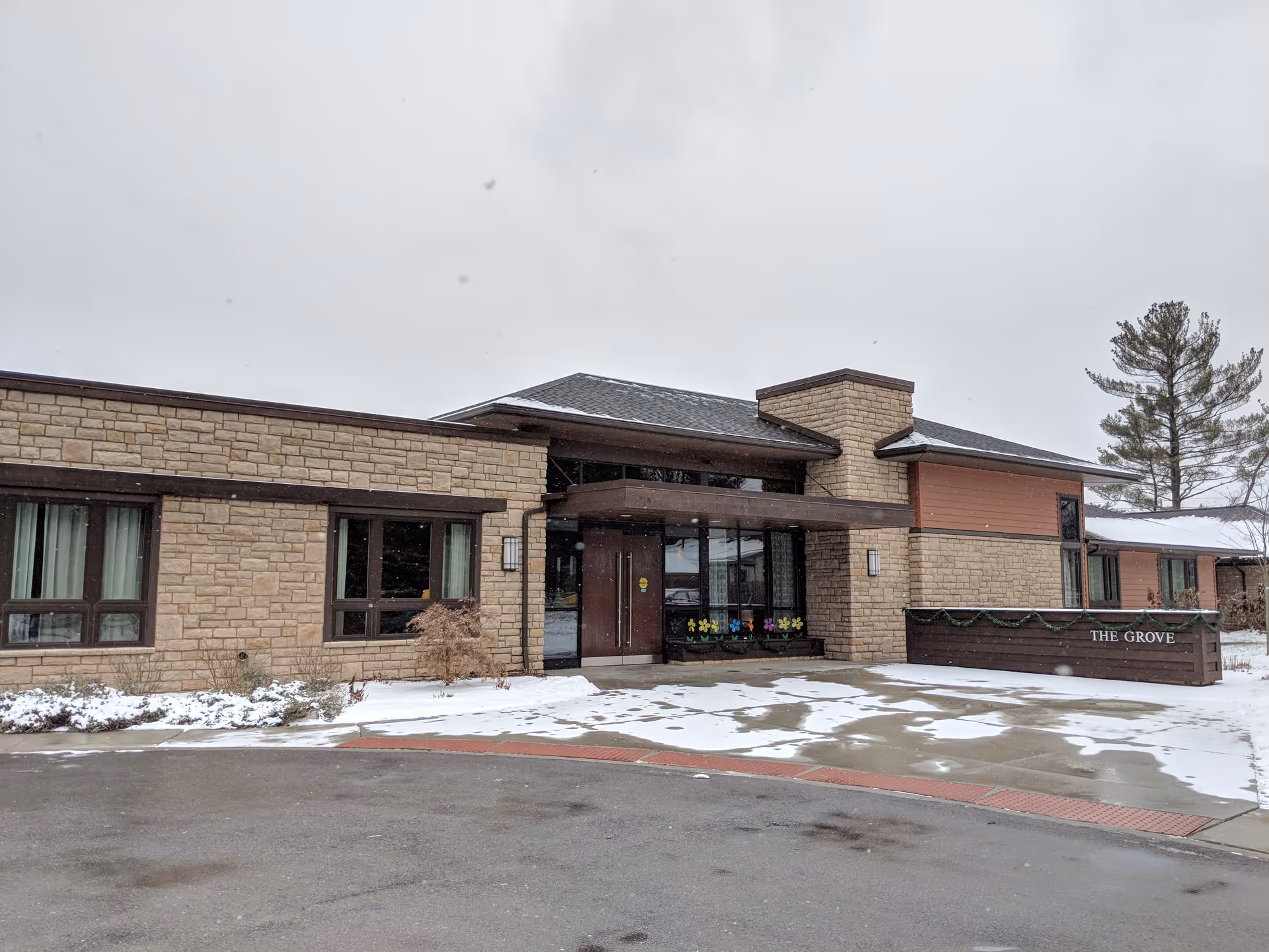 Brick senior living facility entrance with snow and a THE GROVE sign