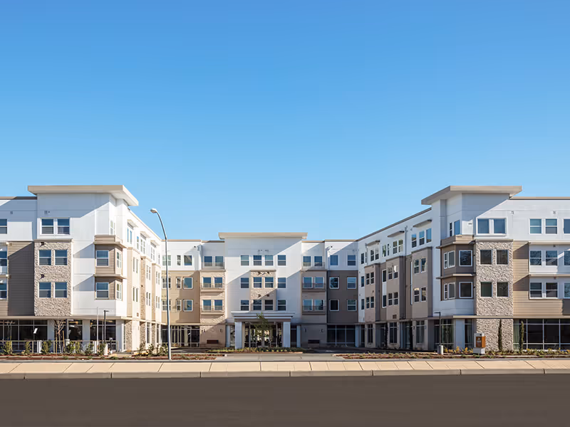 Front view of a modern four-story senior living building with a symmetrical facade, many windows, and a clear blue sky.