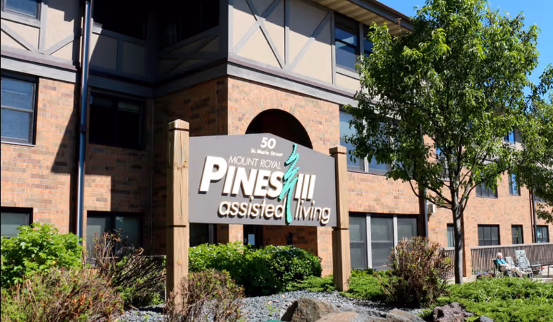 Exterior view of Pines Assisted Living building with sign, brick facade, and landscaping.