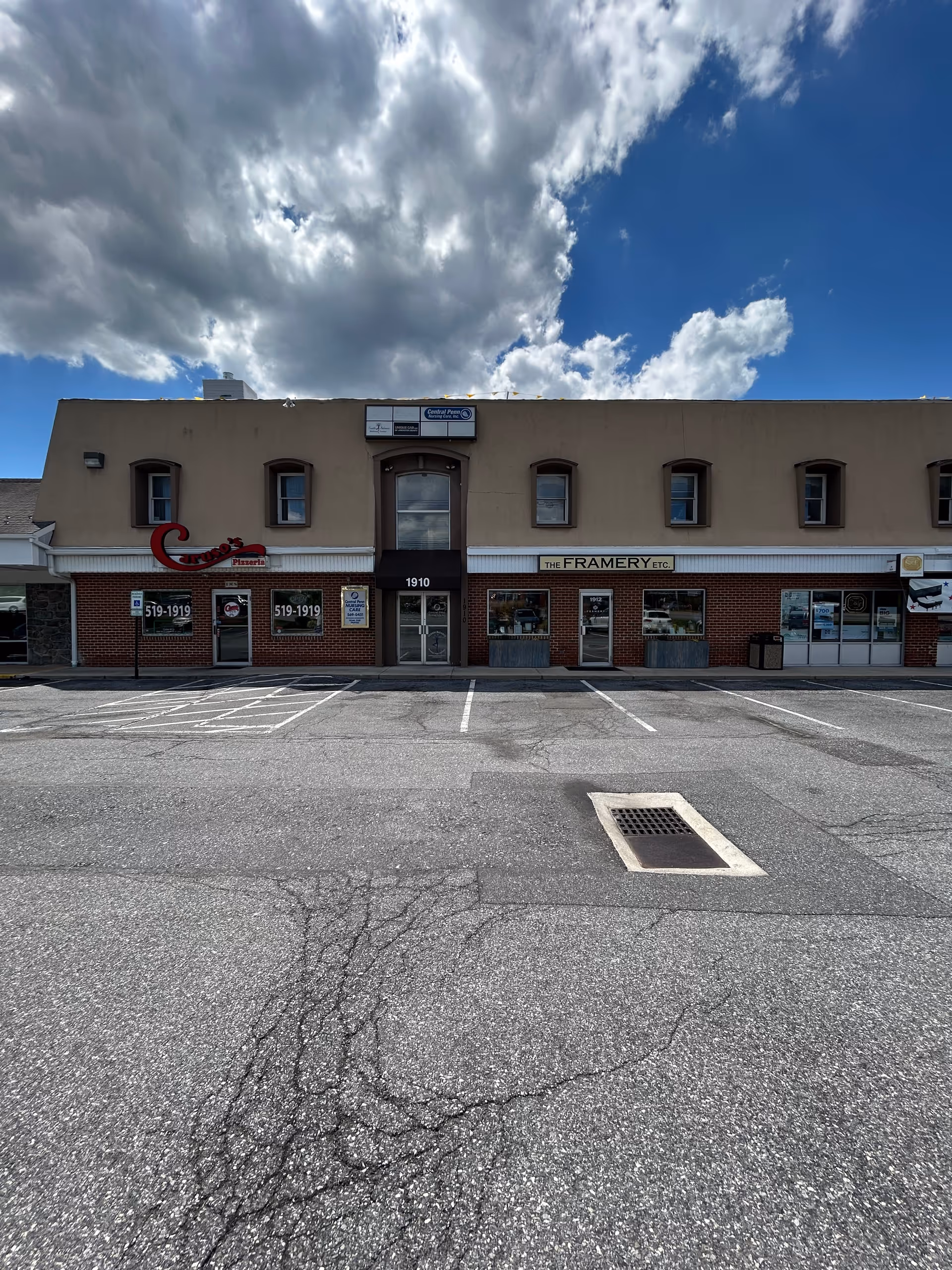 Exterior view of a two-story storefront building with brick lower level and a parking lot.