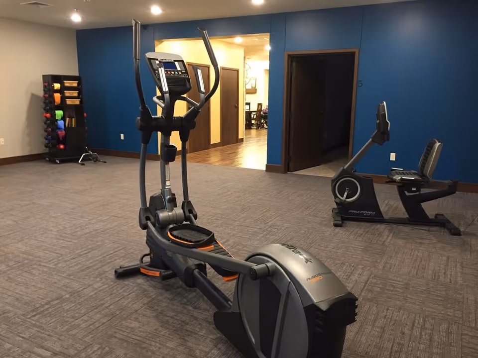 Interior fitness room with elliptical, stationary bike, and weight rack at Pleasant Hills.