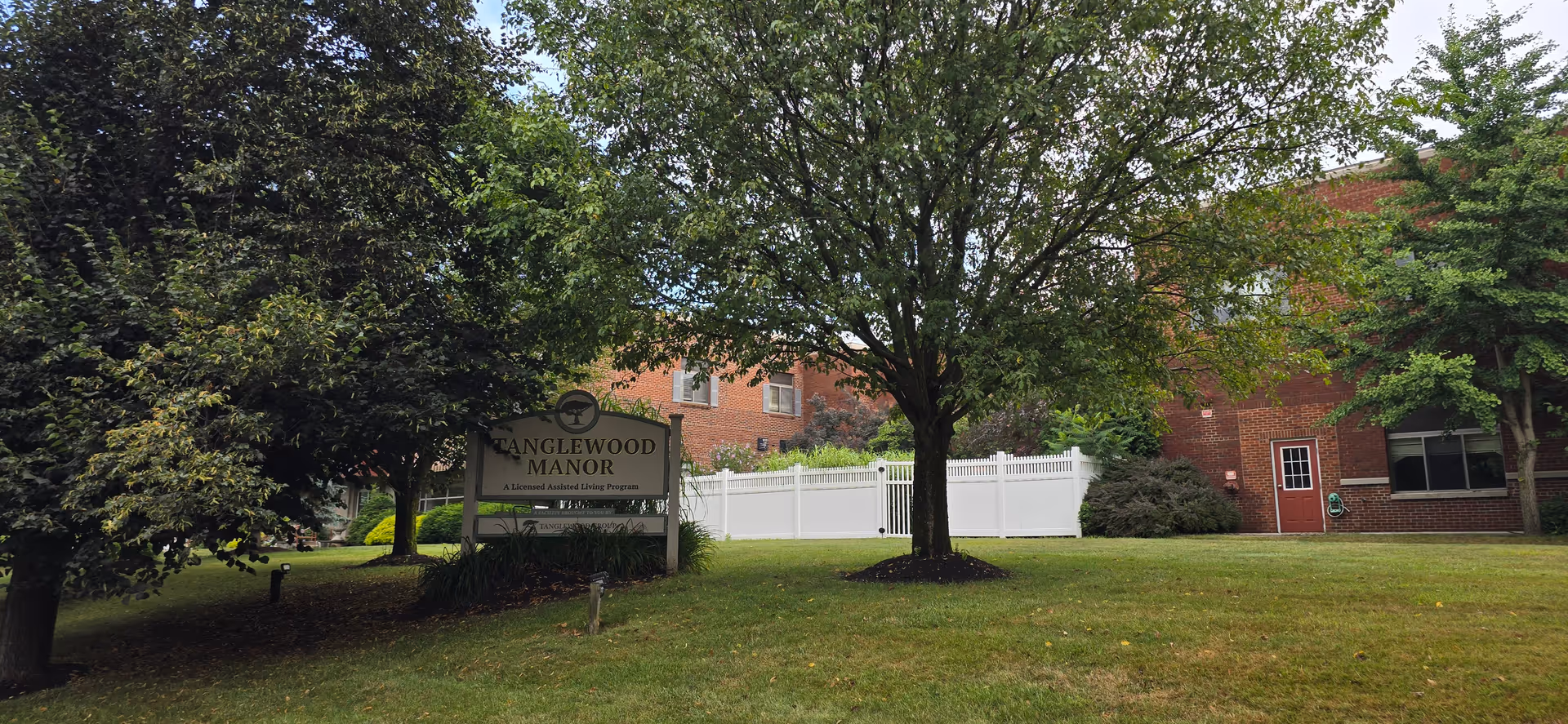 Exterior view of Tanglewood Manor: sign, lawn, trees, and brick building facade.